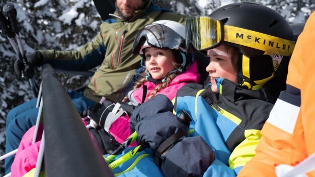 Family on a ski lift with snow-covered trees in the background. | © FW21 / McKinley