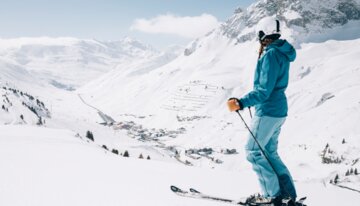 Skifahrerin in blauer Skibekleidung steht auf der Piste und schaut in die Ferne | © Daniel Zangerl, Lech Zürs Tourismus