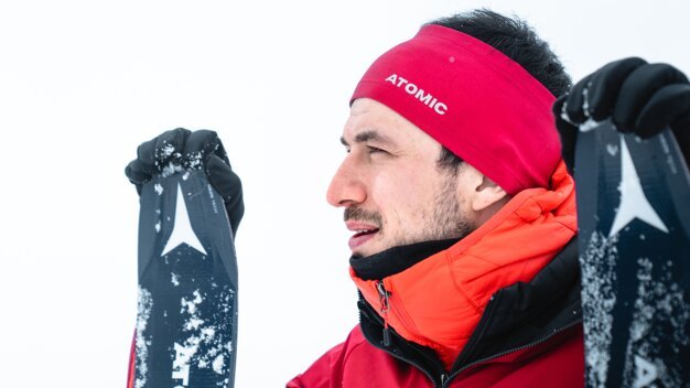 Man with Atomic headband holding skis in the snow. | © ATOMIC