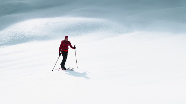 Skier in red jacket and beanie on a snowy slope. | © ATOMIC