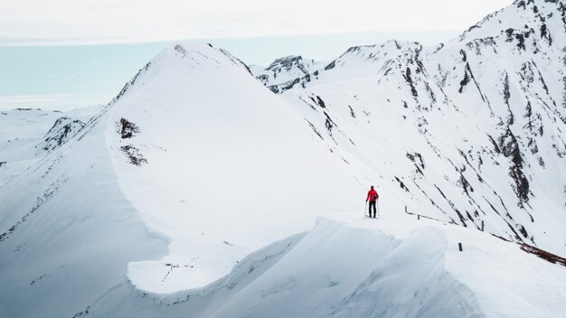 Mountaineer in red jacket on snowy mountain ridge | © ATOMIC