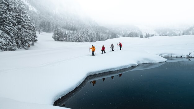 A group of four people snowshoeing next to a lake. | © ATOMIC