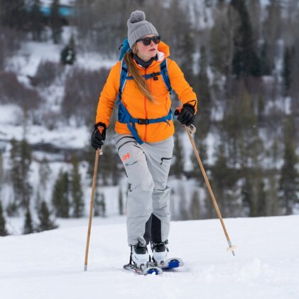Woman snowshoeing, wearing orange jacket and grey hat in the snow. | © Helly Hansen / Cam McLeod