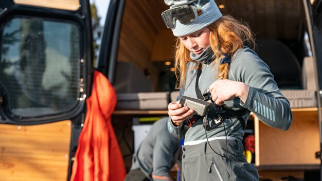 Red-haired woman operating a device in front of a van. | © Helly Hansen / Cam McLeod