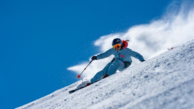 Skier carving through powder snow against a blue sky. | © Helly Hansen / Cam McLeod