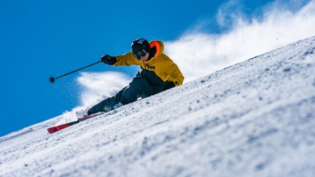 Skier in yellow jacket skiing down a snowy slope. | © Helly Hansen / Cam McLeod