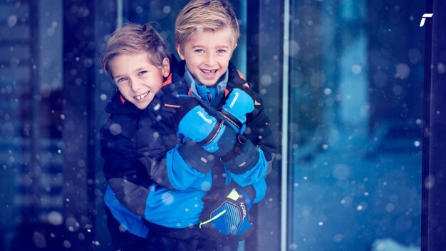 Two smiling boys hugging in the snow wearing Reusch gloves. | © Reusch