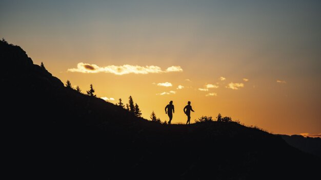 Silhouette of two people walking on a hill at sunset. | © Rossignol / Louis Garnier