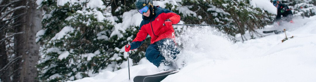 Skier carving through deep powder in a snowy forest. | © Rossignol / Cam McLeod 2021