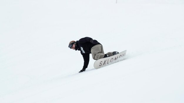 Snowboarder riding on snow, bracing with one hand. | © SALOMON