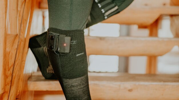 Person mit beheizbaren Socken auf einer Holztreppe. | © Thermic / Loic Schutz