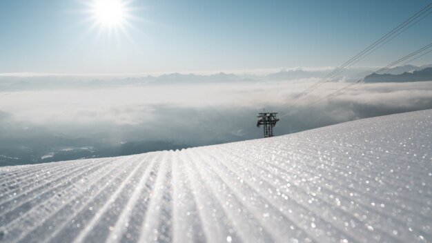 Groomed ski slope with a ski lift station and mountain panorama under a bright sun. | © McKINLEY
