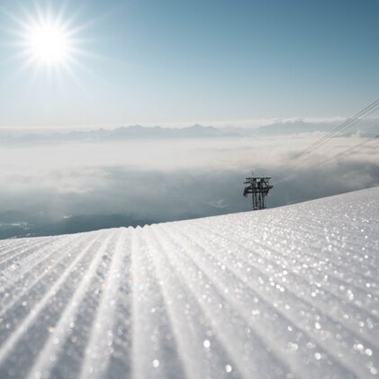 Vorbereitete Skipiste mit Skiliftstation und Bergpanorama unter strahlender Sonne. | © McKINLEY