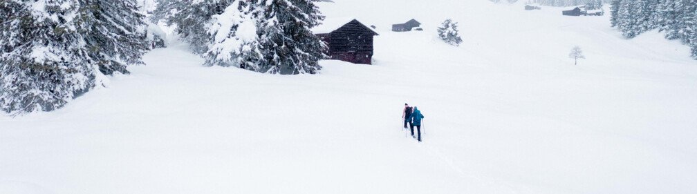 Two people hiking through a snowy winter landscape. | © McKINLEY