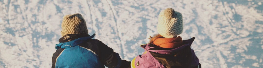 Two children sitting in the snow, holding hands.
