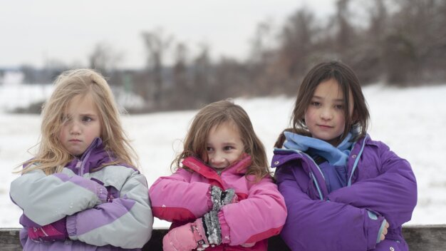 Three girls in winter jackets standing outside in the snow.