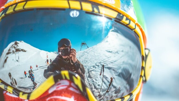 Reflection of a skier with a camera in ski goggles.