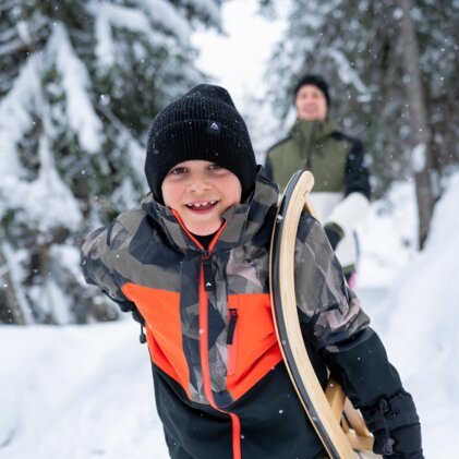A smiling boy carrying a sled in the snow. | © McKINLEY