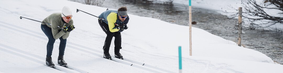 Zwei Langläufer auf einer verschneiten Loipe neben einem Fluss. | © INTERSPORT International Corporation GmbH