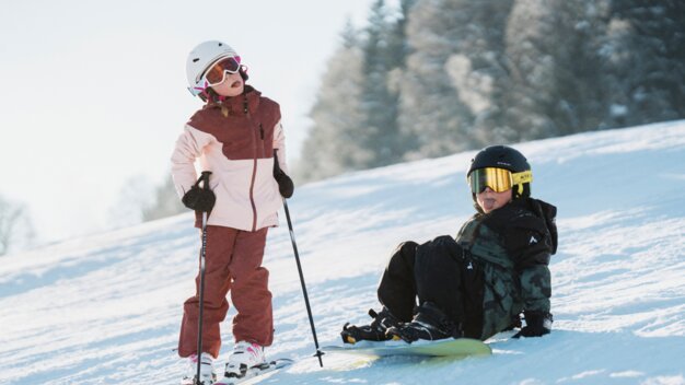 Two children skiing and snowboarding in the snow. | © INTERSPORT International Corporation GmbH