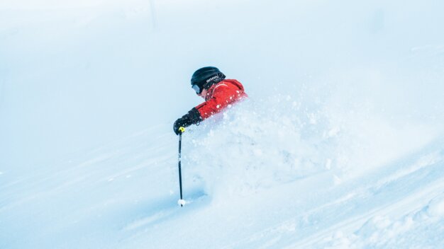 Skifahrer in roter Jacke fährt durch Tiefschnee.