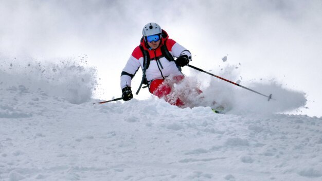 Skifahrer im Tiefschnee mit Schneestaub.