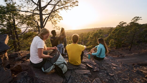 Gruppe von Wanderern macht eine Pause auf einem Felsen bei Sonnenuntergang.