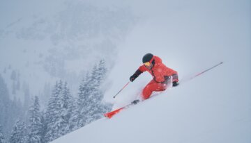 Skifahrer in roter Kleidung fährt einen verschneiten Hang hinunter. | © INTERSPORT International Corporation GmbH