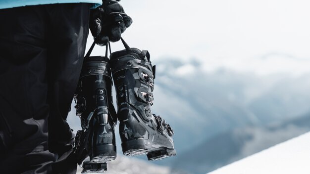 A pair of ski boots being held by a person against a snowy mountain backdrop. | © Atomic Austria GmbH