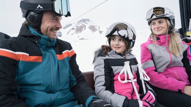 Famille utilisant un télésiège, tous portant casques et lunettes de ski. | © IIC/McKINLEY