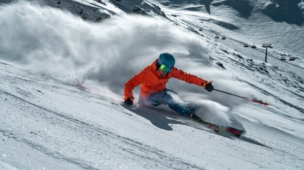 Skifahrer in orangefarbener Jacke fährt einen verschneiten Hang hinunter. | © Fischer Sports GmbH