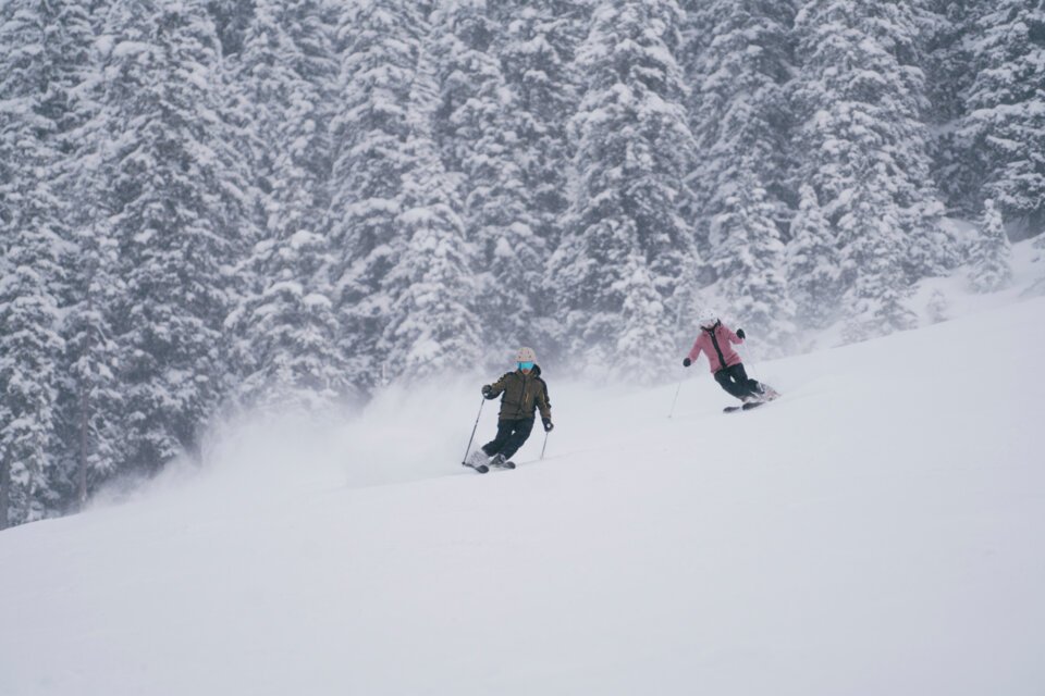 Two skiers on a snowy slope with a forested backdrop. | © INTERSPORT International Corporation GmbH