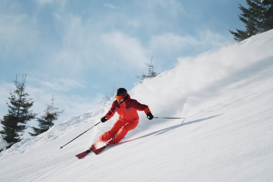 Skier in red suit skiing down a snowy slope. | © INTERSPORT International Corporation GmbH