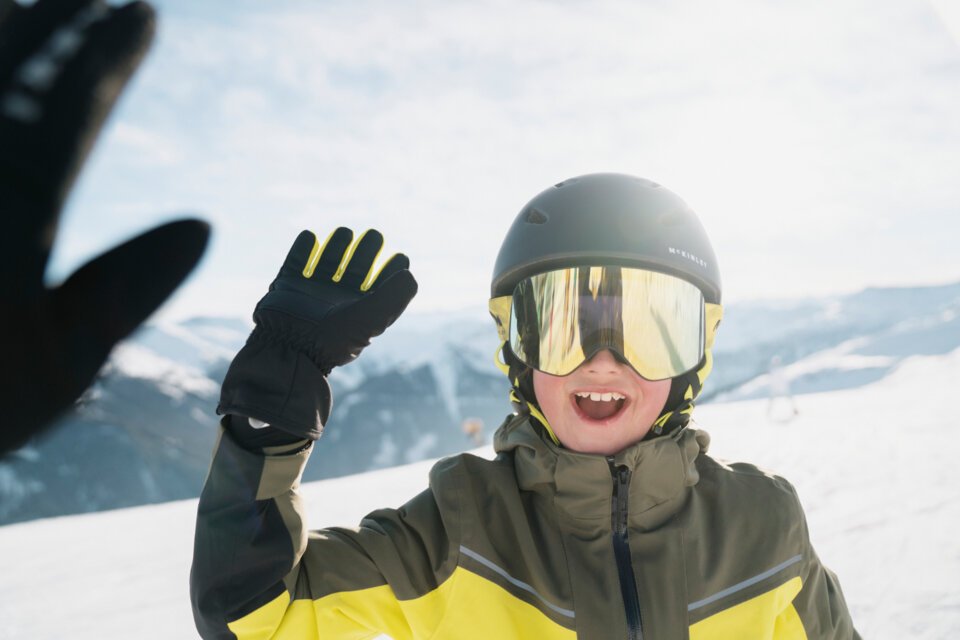 Junge mit Skibrille und Helm winkt auf einer Skipiste. | © INTERSPORT International Corporation GmbH