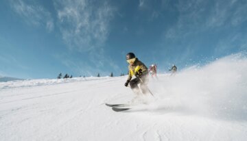 Skifahrer auf einer schneebedeckten Piste bei strahlend blauem Himmel | © INTERSPORT International Corporation GmbH