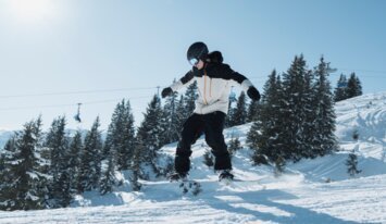 Snowboarder jumping in the air against a snowy backdrop. | © INTERSPORT International Corporation GmbH
