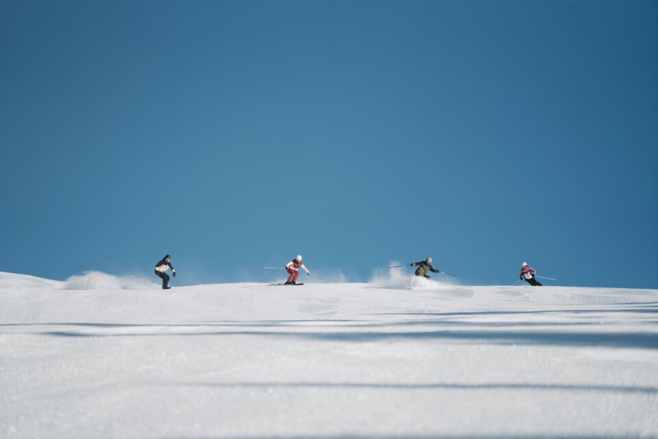 Gruppe von Skifahrern auf einer schneebedeckten Piste unter blauem Himmel. | © INTERSPORT International Corporation GmbH