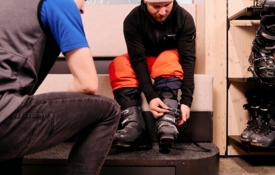 Man fastening ski boot with assistance from a salesperson.