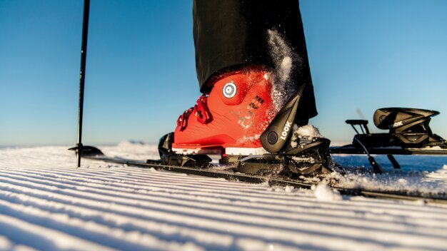 Red ski boot in binding on groomed slope | © ROSSIGNOL