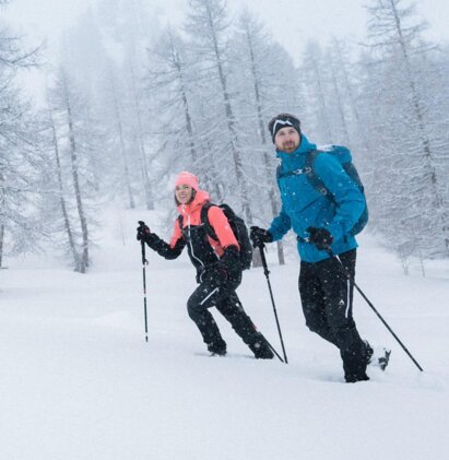 Two people snowshoeing in a snowy forest with poles. | © IIC/McKINLEY
