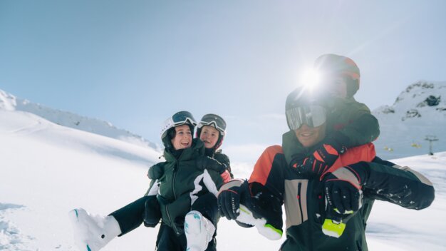 Père portant deux enfants sur ses épaules dans la neige.