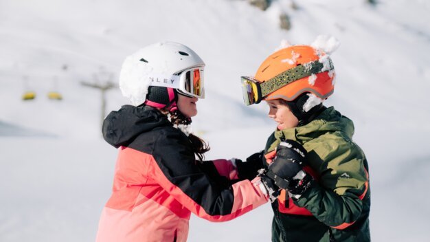 Deux enfants en tenue de ski dans la neige.