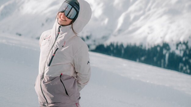 Woman in snowboard gear kneeling in the snow with mountain backdrop