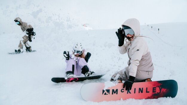 Two snowboarders and one person in the background on a snowy slope.