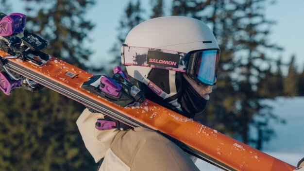 Person wearing ski helmet and carrying skis.