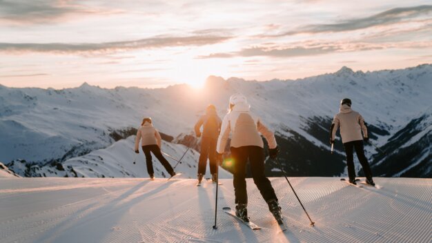 Group of skiers skiing down a mountain at sunset.