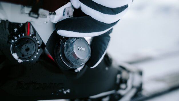 Close-up of a ski boot with a BOA closure and a hand in a striped glove