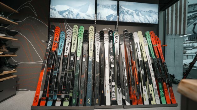 Row of skis of various brands and models in a store.