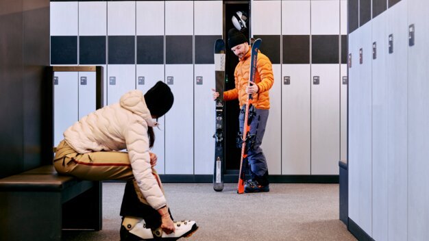 Two people preparing to ski in a ski room. | © ARMIN WALCHER