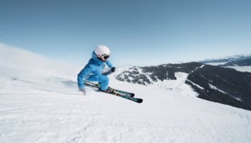 Skier in blue jacket skiing down a snowy slope. | © INTERSPORT International Corporation GmbH